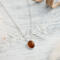  A playful 18" sterling silver necklace with a 10mm Baltic amber oval pendant on a light wood table, surrounded by soft decor. 
